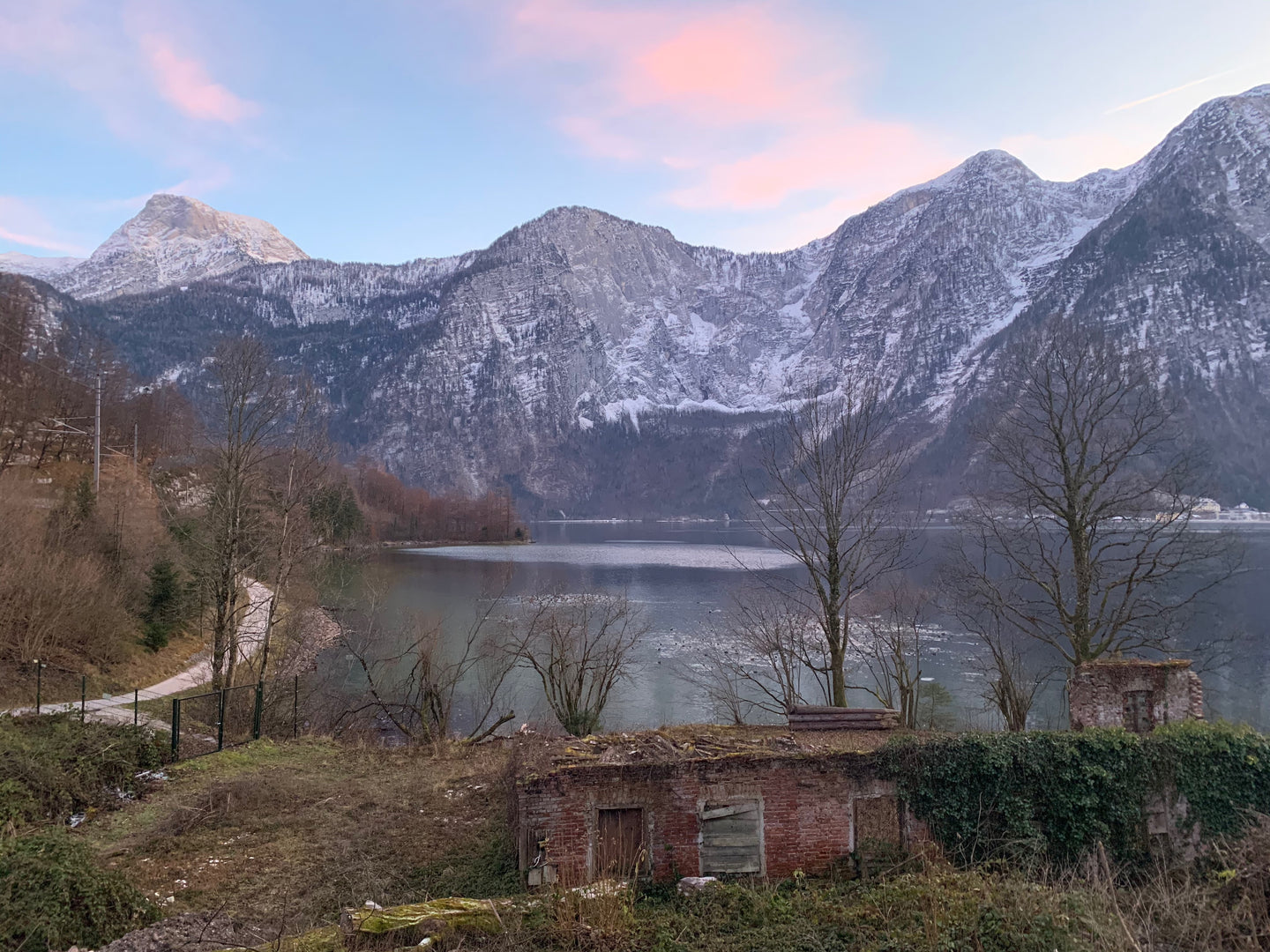 image of snowy mountain range with a lake in front and a small rustic shed and a road to the left going toward the mountains